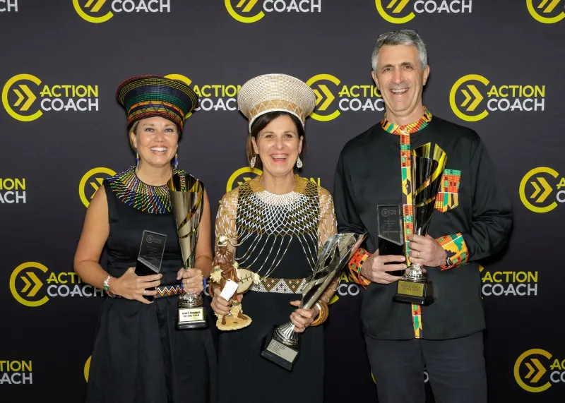 Three smiling award winners in traditional African attire hold trophies at ActionCoach event